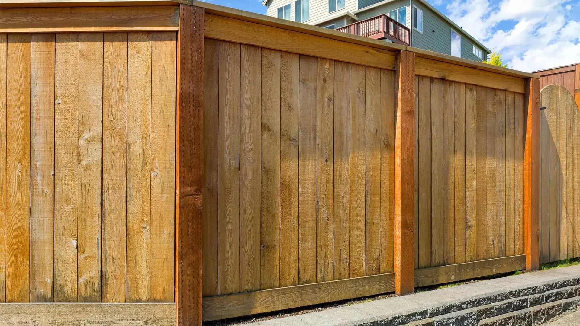 A privacy wood fence beautifully stained with a house on the background